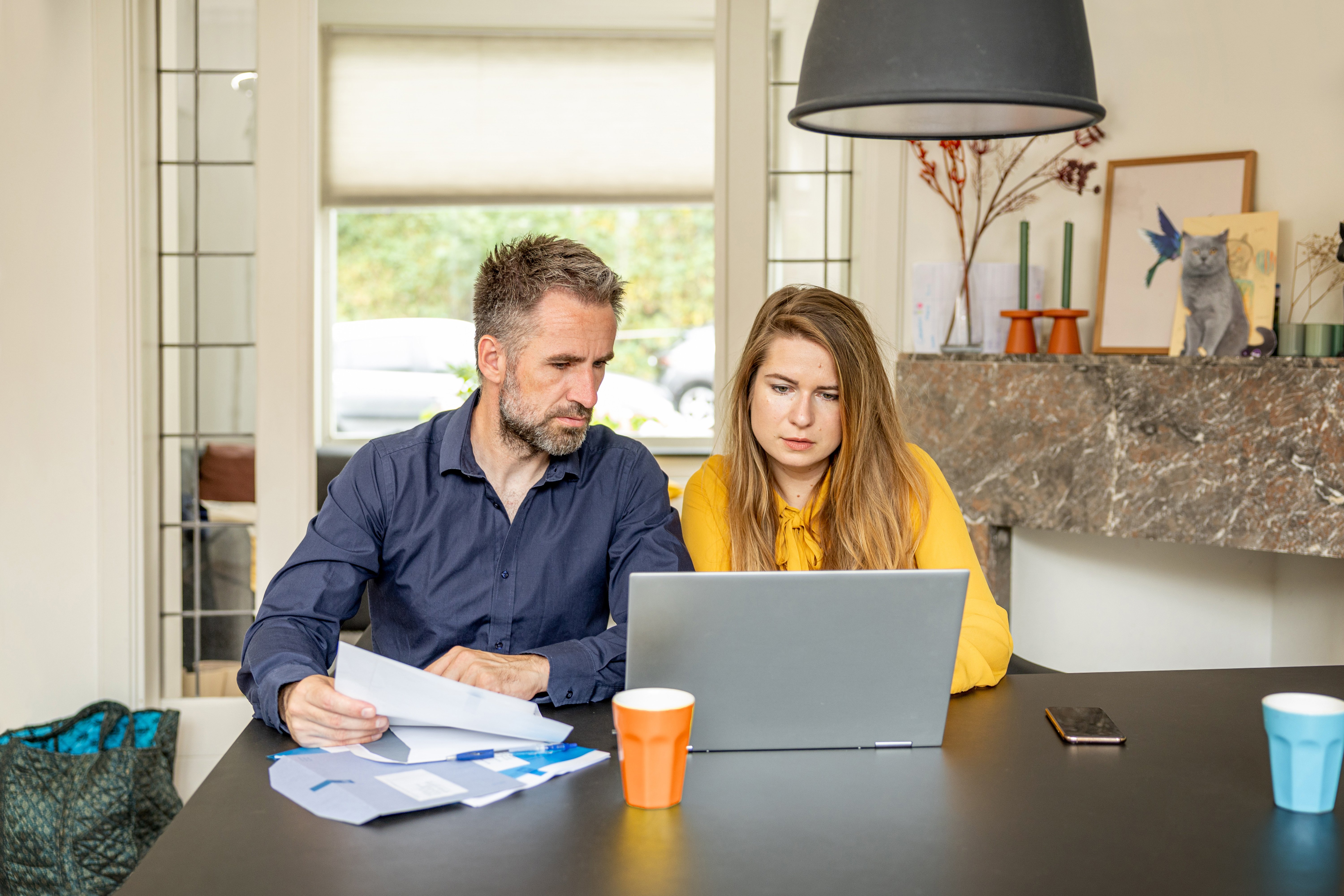 Man en vrouw kijken naar hun laptop met Belastingdienst brieven in de hand